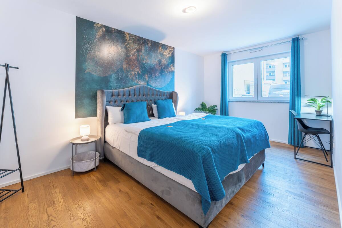 Ein modernes Schlafzimmer mit einem großen Bett, einem Schreibtisch und einem Fenster mit Vorhängen.