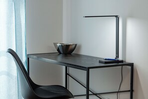 A modern desk with a black metal frame, a black desk lamp, a blue pen, and a metallic bowl.
