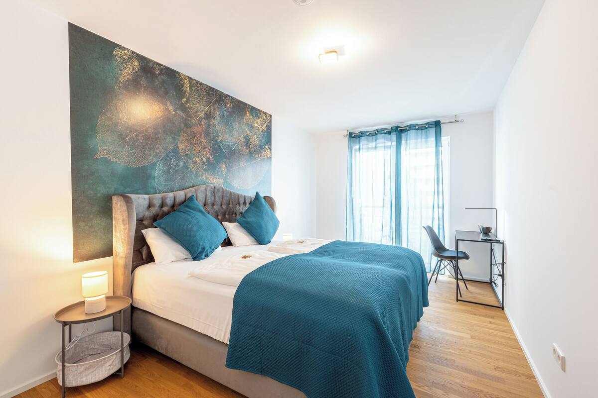 Ein Schlafzimmer mit einem Bett, einem Nachttisch, einem Schreibtisch und einem großen abstrakten Gemälde an der Wand.