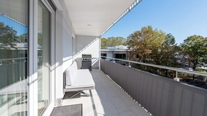 Een balkon met een matras, een barbecue en uitzicht op bomen en gebouwen.