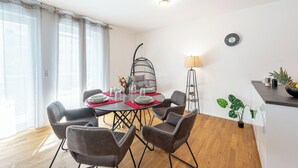 Een eethoek met een tafel voor vier personen, een hangstoel, een klok, een lamp en een potplant.