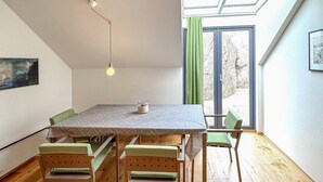 Een eetruimte met een tafel en stoelen, een hanglamp, een raam met gordijnen en een ingelijst kunstwerk aan de muur.