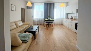 A living room with a sofa, coffee table, and dining table with chairs. There is a kitchen area with cabinets and a stove. - Nice apartment in Koszalin with WiFi (Koszalin)