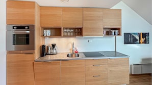 Een moderne keuken met houten kastjes, een inbouwoven, een koffieapparaat en een spoelbak.