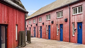 Een rij rode gebouwen met blauwe deuren en ramen, een betegelde grond en een houten omheining.