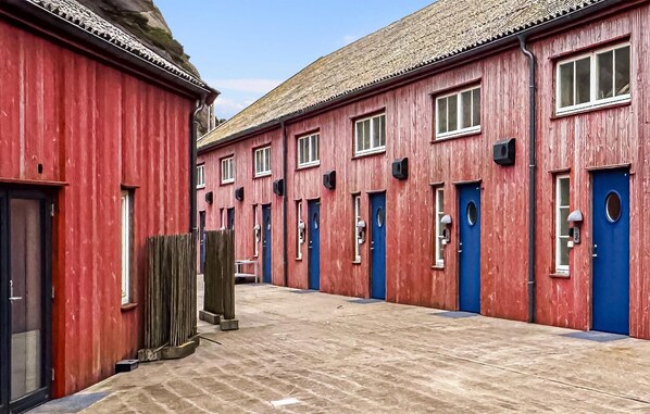 A row of red buildings with blue doors and windows, a tiled ground, and a wooden fence. - Nice apartment in Søgne with house sea view (Søgne)