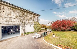 A building with a covered patio area, outdoor seating, and a garden with red flowering bushes. - Stunning apartment in Treignac with WiFi (Treignac)