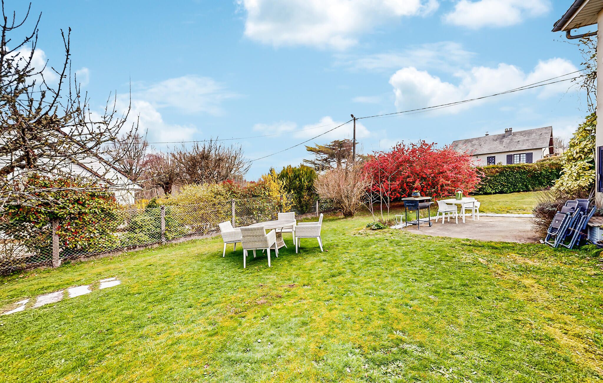 Ein Garten mit Esstisch und Stühlen, einem Grill und einem blühenden roten Strauch.