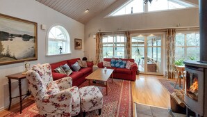 A spacious living room with a fireplace, red sofas, floral armchairs, and large windows.