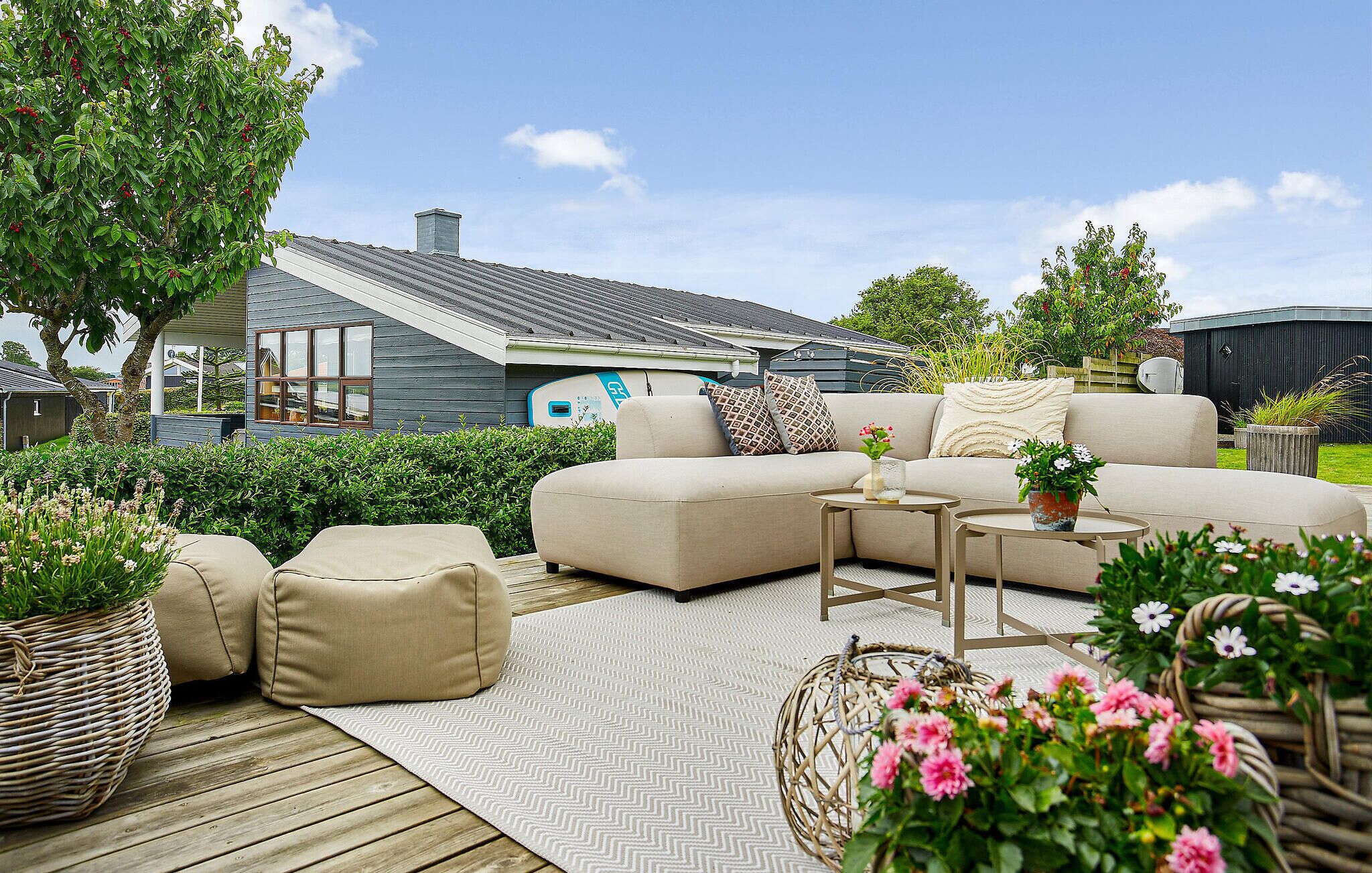 An outdoor seating area with a sofa, ottomans, and a coffee table. There are potted plants and a wooden deck.
