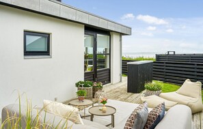 En modern uteplats med en soffa, bord och krukväxter.