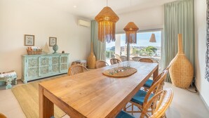 Un espace repas avec une table en bois, des chaises en osier et des luminaires suspendus.