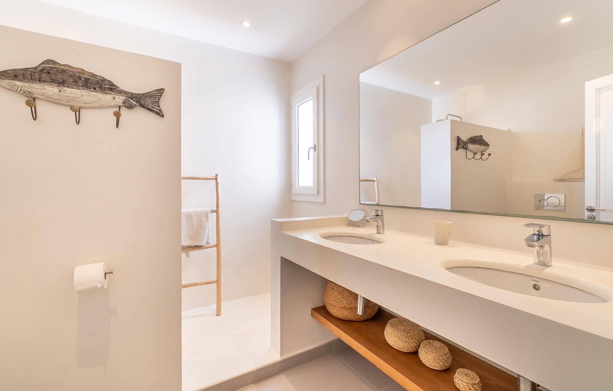 Un baño moderno con dos lavamanos, un espejo grande y un estante de madera con cestas.