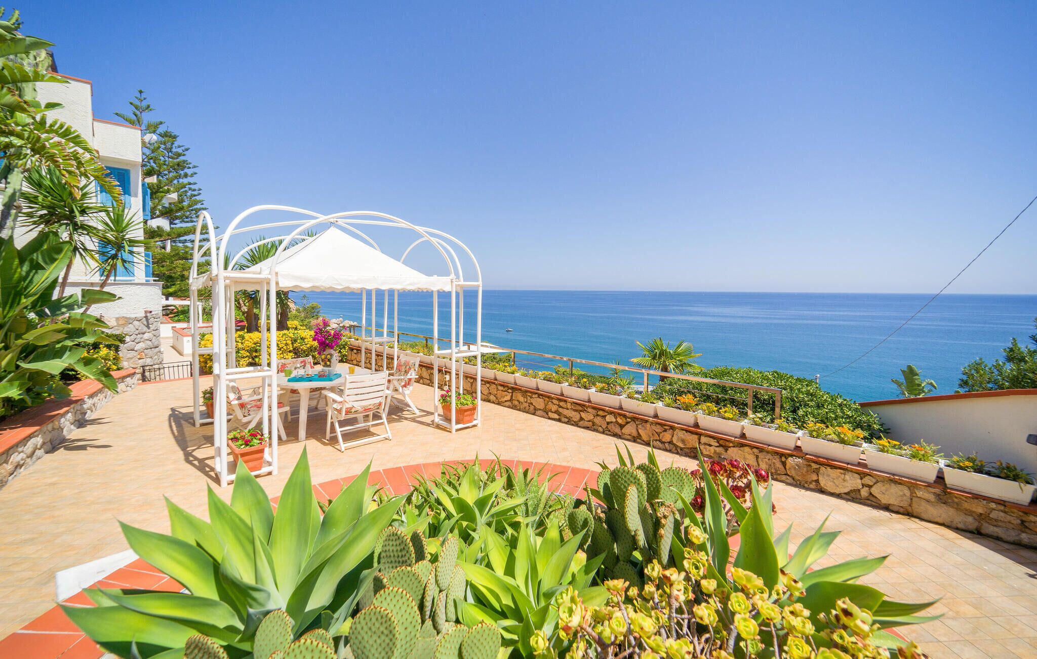 Un patio con un pabellón blanco, mobiliario exterior y vista al mar.