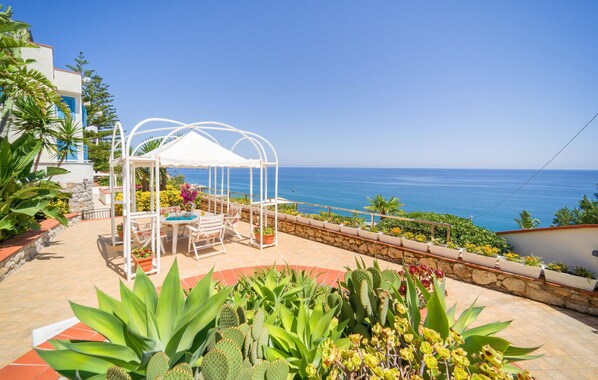 A patio with a white gazebo, outdoor seating, and a view of the sea.