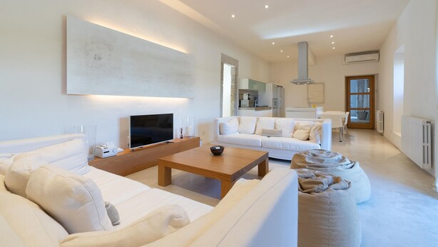 A modern living room with a flat-screen TV, a wooden coffee table, and two white sofas.