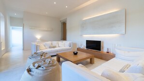 A modern living room with a white sofa set, a coffee table, and a flat-screen TV.