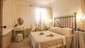 Un dormitori amb llit, taules de nit, un mirall, una finestra amb cortines i un penjoll.