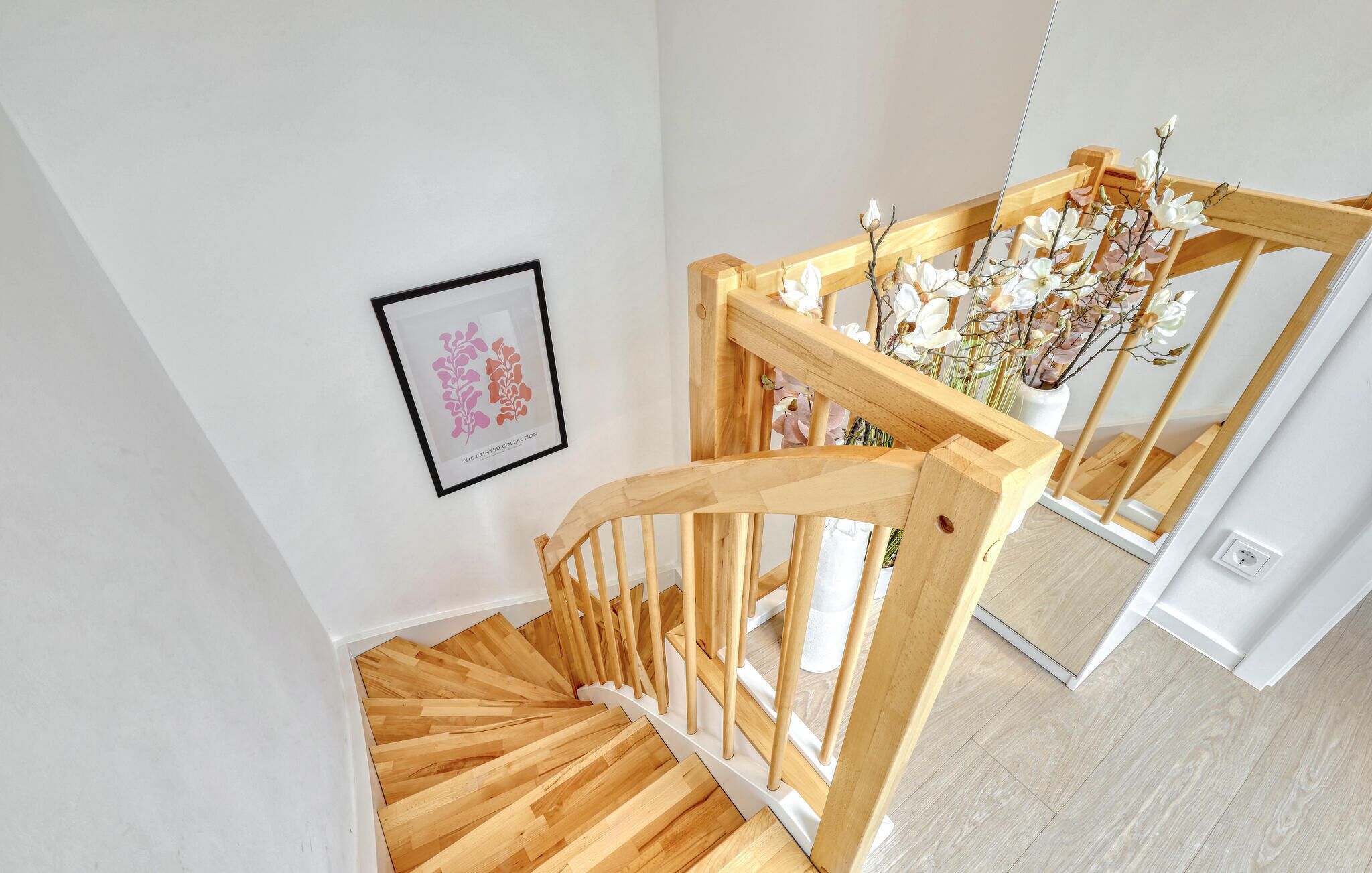 A wooden staircase with a white wall and a framed botanical print.