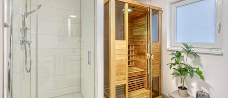 Une salle de bain moderne avec une douche à l’italienne en verre, un sauna en bois et une plante en pot.