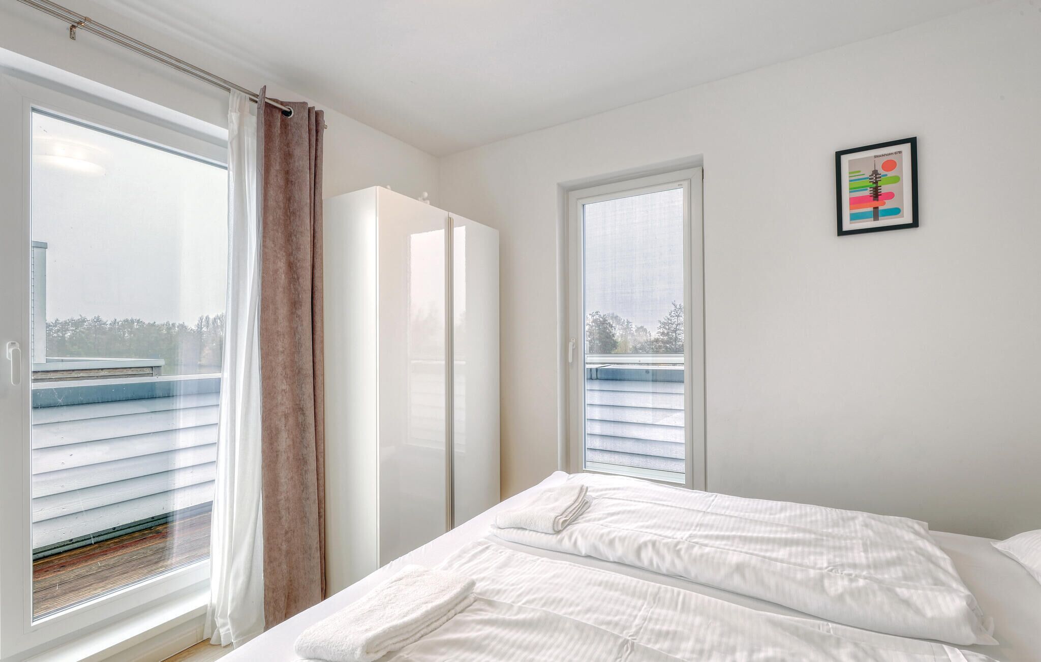 Une chambre à coucher avec un lit, deux fenêtres, une porte et un tableau encadré au mur.