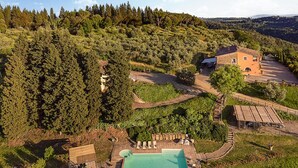 Vista aérea de uma propriedade com piscina, deck de madeira e uma casa rodeada por uma floresta densa.