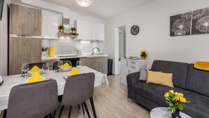 A modern kitchen with white cabinets, a dining table set for four, and a grey sofa with yellow cushions. - Cozy apartment in Dramalj with house sea view (Dramalj)
