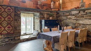 Une salle à manger rustique avec un mur en pierre, une table en bois dressée pour six personnes et un piano.