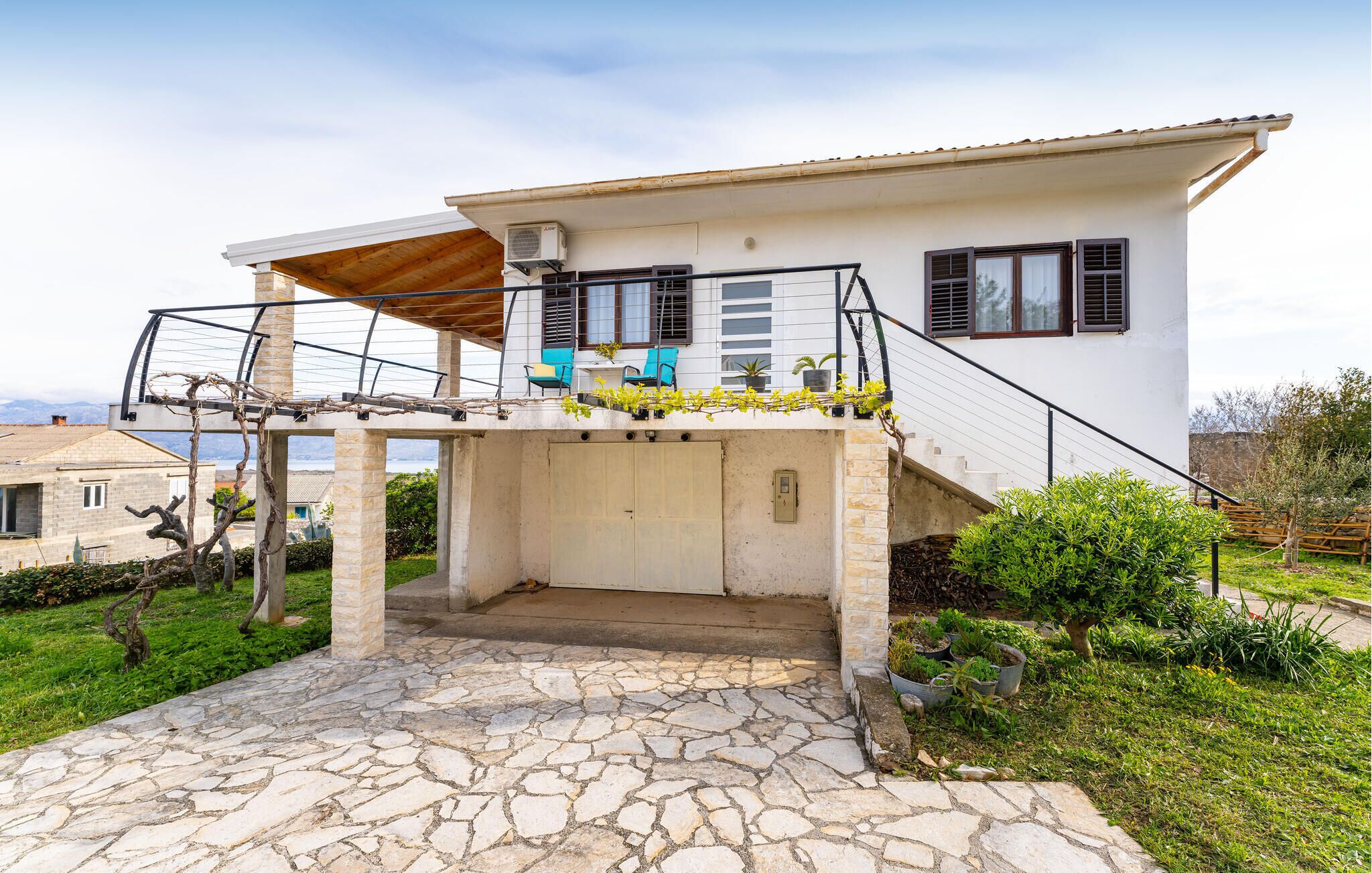 A two-story house with a stone-paved entrance, a balcony with chairs, and a view of the surrounding landscape.