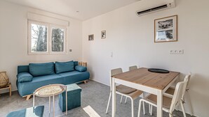 A modern living room with a blue sofa, a wooden dining table with chairs, and a large window with a view of trees.