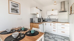 A modern kitchen with white cabinets, a microwave, and a sink. There is a dining table with black placemats and glasses.