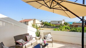A balcony with wicker furniture, a table, and a large umbrella.