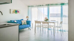 A modern kitchen with a blue sofa, white chairs, and a dining table.