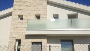 A modern building with a stone facade, a glass balcony, and a chain-link fence.