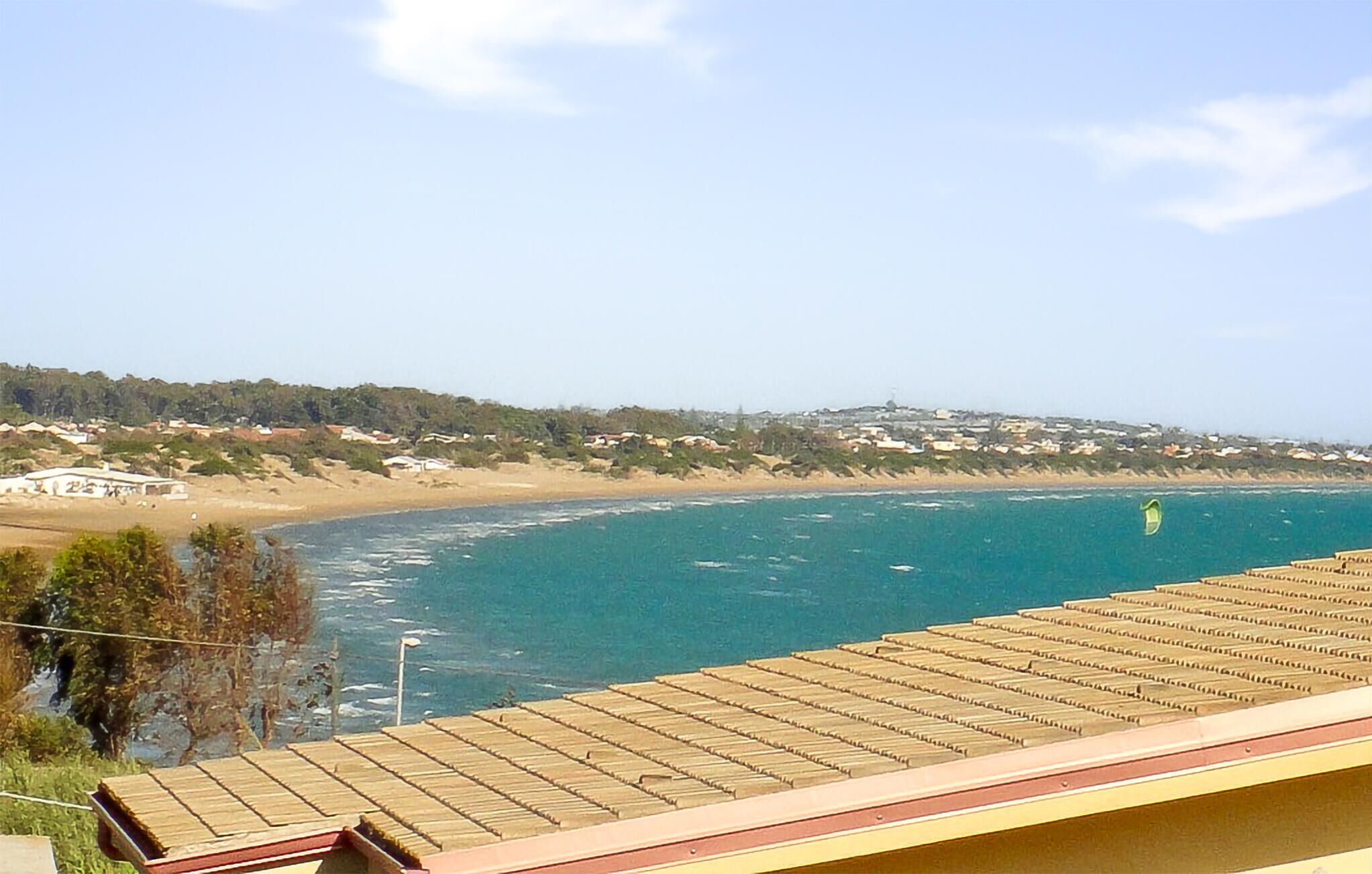 A coastal view with a beach, a building with a tiled roof, and a distant town.