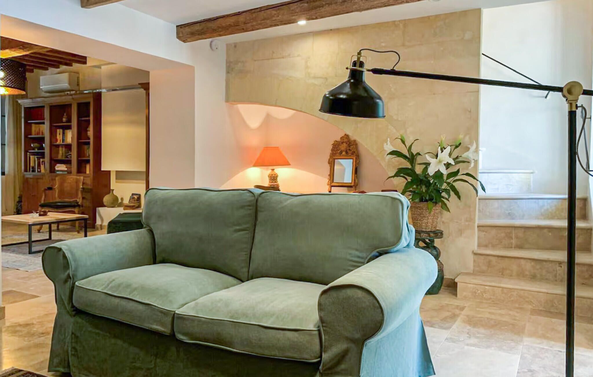 A living room with a green sofa, a floor lamp, a table lamp, a bookshelf, and a potted plant.