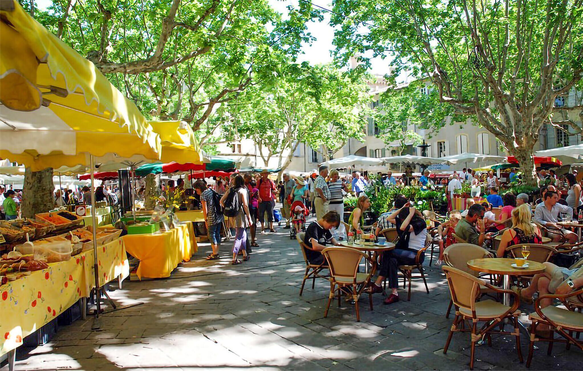 Un marché en plein air avec des étals de nourriture et des tables où les gens prennent leur repas.