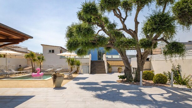 Un patio con piscina, sillas de descanso y una escalera que lleva a un edificio.