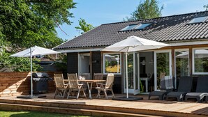 En overdækket terrasse med træterrasse, udendørs møbler og grill.