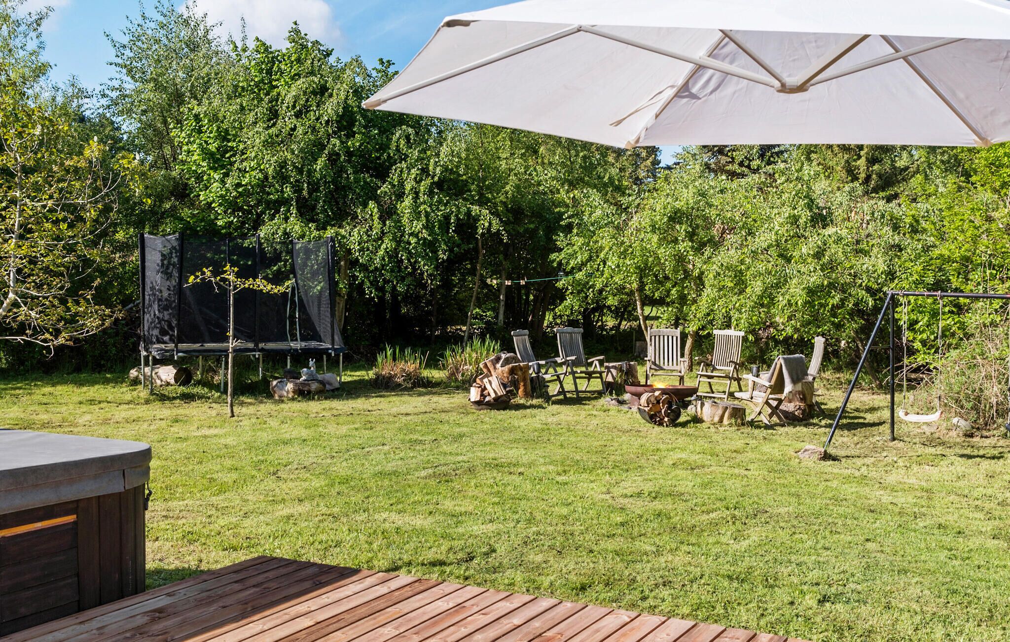 A backyard with a trampoline, outdoor seating, and a hot tub.