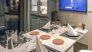 Une table à manger dressée avec des verres à vin, des assiettes et des couverts, et un téléviseur diffusant un message en arrière-plan.