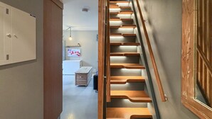 Un escalier avec des marches en bois et une rampe, menant à une pièce où se trouvent un lit et un téléviseur fixé au mur.