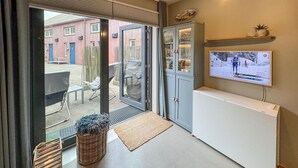 Un espace d’accueil avec un téléviseur diffusant un événement sportif, un panier en osier et une petite table avec des chaises.