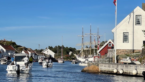 Un port avec des bateaux, un grand voilier et un bâtiment blanc surmonté d’un toit rouge.