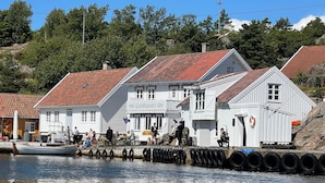 Un bâtiment blanc surmonté d’un toit de tuiles rouges, appelé « Landhandel », situé près d’un quai où se trouvent un bateau et des personnes.