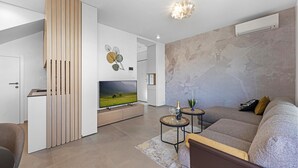 A modern living room with a flat-screen TV, a sofa, a coffee table, and a decorative wall piece.