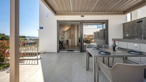 A modern outdoor patio with a dining table set for two, a grill, and a view of the sea.