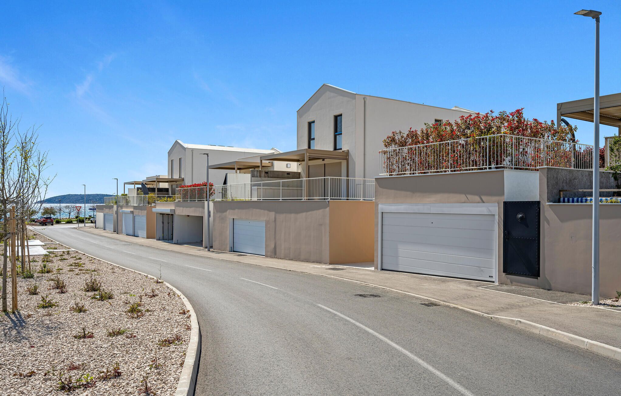 A modern residential building with multiple garage doors, a curved road, and a clear view of the sea in the background.