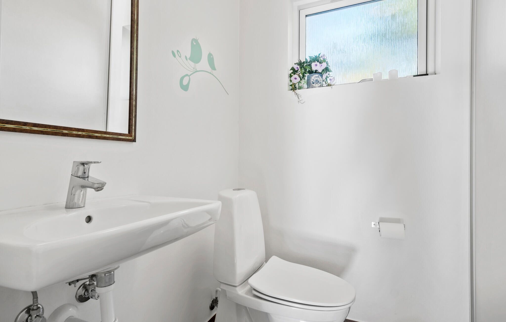 A bathroom with a white sink, toilet, and a window with a view of greenery.