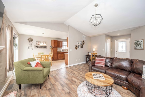 A living room with a green armchair, a brown leather sofa, a round coffee table, and a chandelier.
